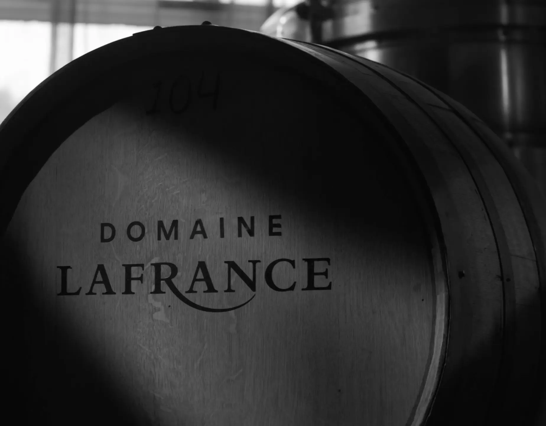 Close-up of a wooden wine barrel in a winery, with the brand name Domaine Lafrance visible in black and white.